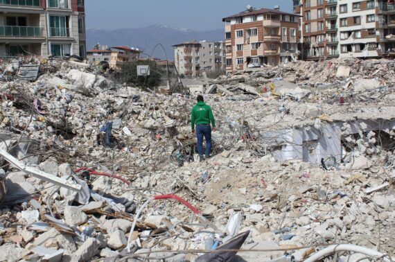 A man wearing GOAL green hoodie standing in the midst of rubble from collapsed buildings after Turkey-Syria Earthquakes 2023